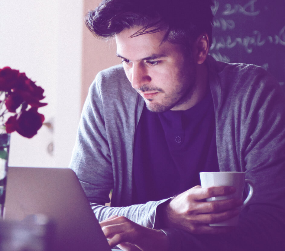 Foto de um homem usando o notebook segurando uma xícara branca.