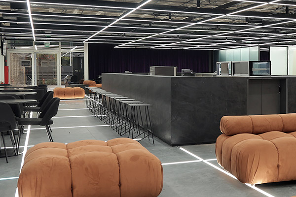 Imagem do foyer com o café-bar em destaque. Ao redor, pufes, mesas e cadeiras.