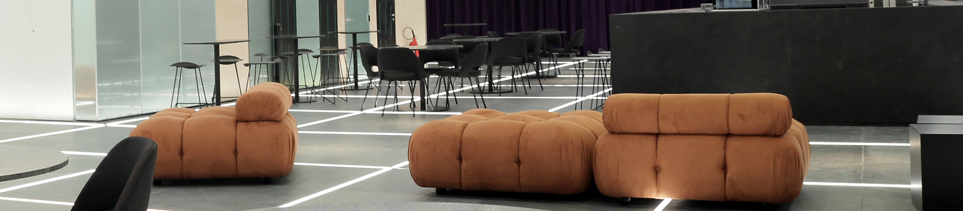 Imagem do moderno hall de entrada do Teatro Vivo com os pufes de cor caramelo em primeiro plano.