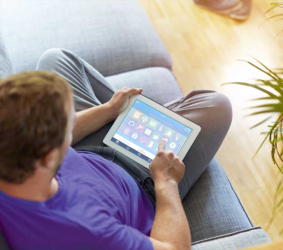 Imagem de um homem no sofá, configurando uma rotina de dispositivos inteligentes. 