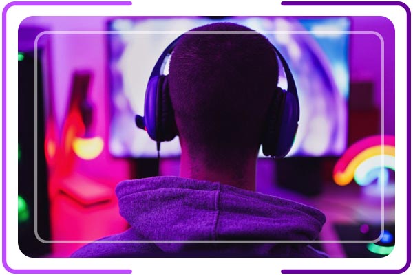 Imagem de um jovem de costas. Ele está de headset e utilizando o computador.