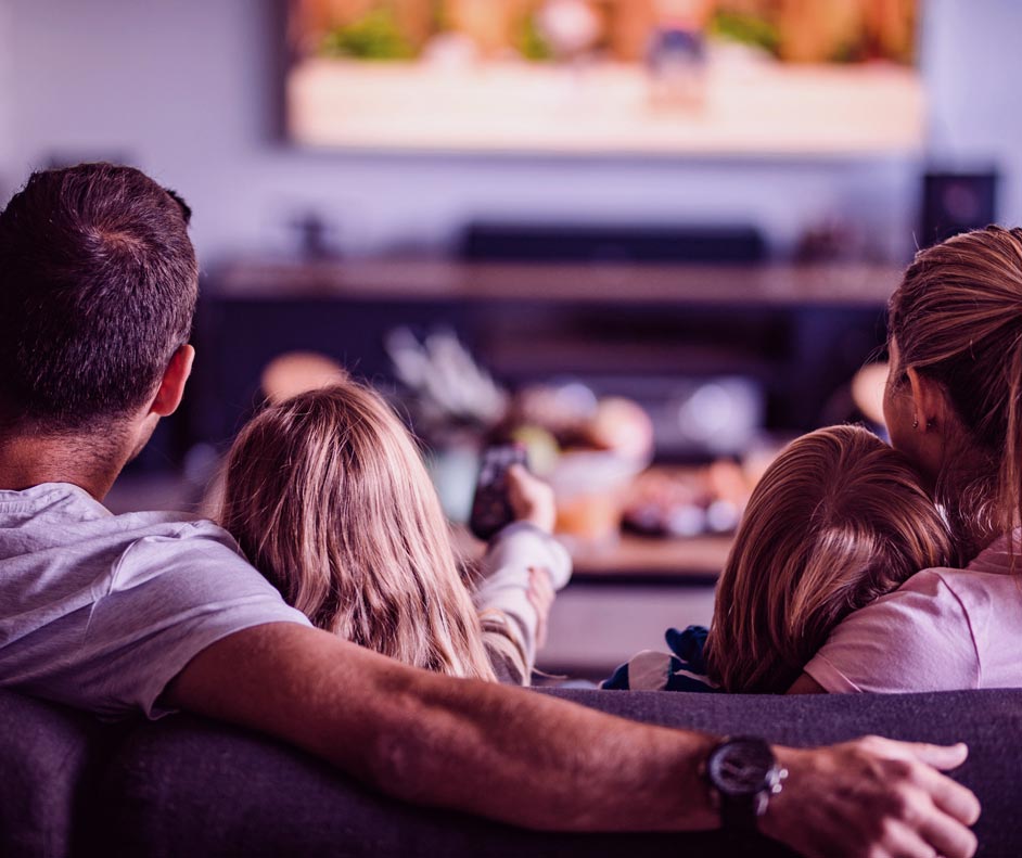 Família reunida e sentada no sofá com o controle direcionado para TV para assistir Globoplay