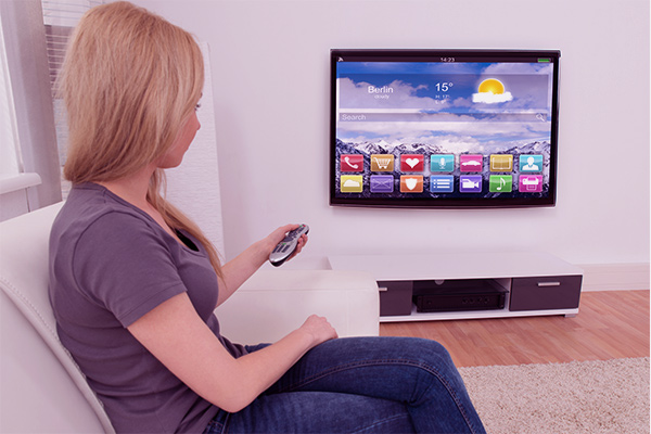 Imagem de uma mulher no sofá, apontando o controle remoto para a TV.