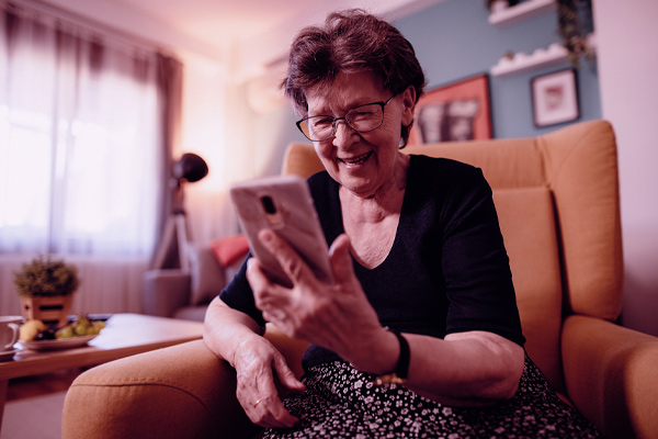 Imagem de uma senhora olhado para a tela do celular e sorrindo.