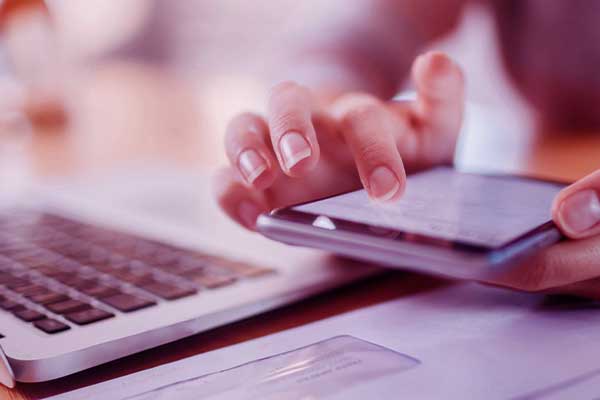 Mão mexendo no celular configurando a atualização de software e um notebook ao lado,.