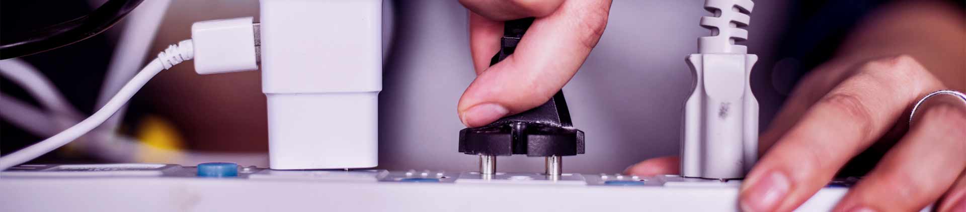 Pessoa conectando aparelho bivolt em filtro de linha. Dois outros cabos estão conectados