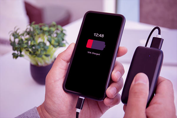 Homem segurando um celular e um power bank carregando celular com pouca bateria