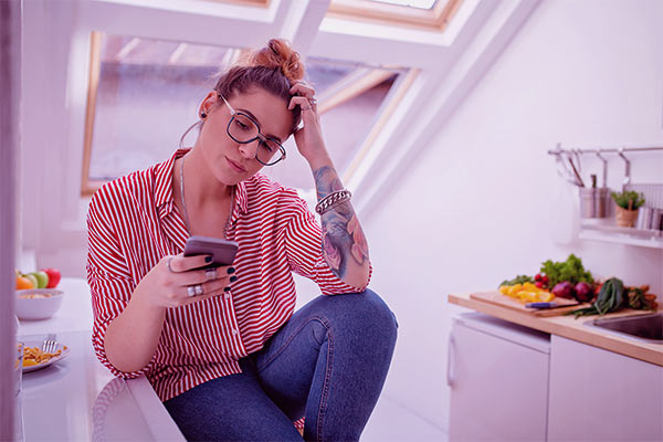 Mulher com a mão na cabeça e com a outra segurando o celular travando