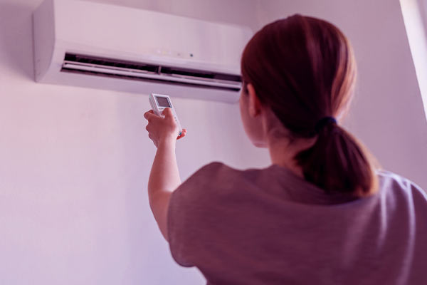 Mulher segurando o controle do ar-condicionado para desligá-lo e economizar energia