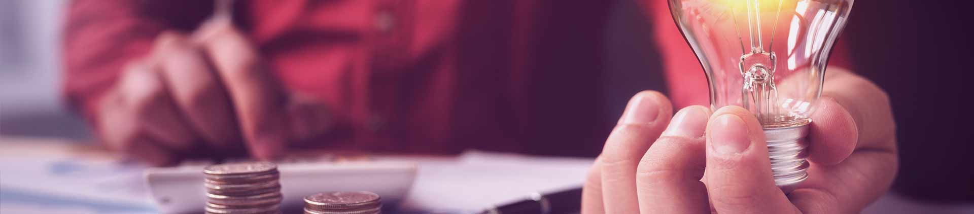 Pessoa segurando lâmpada enquanto faz contas na calculadora. Ela está vendo como economizar energia