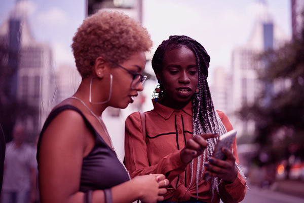 Duas mulheres na rua tentando ligar a cobrar no celular