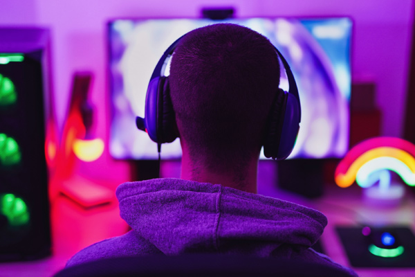 Imagem de um homem de costas, usando fones de ouvido e jogando em um computador.
