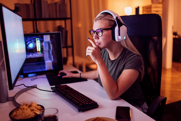 Imagem de uma mulher jogando em um computador e usando fones de ouvido.