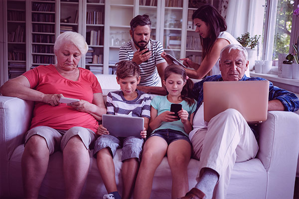 Imagem de uma família reunida no sofá. Cada pessoa usa um dispositivo eletrônico.