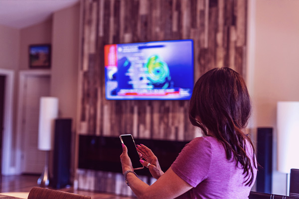 Imagem de uma mulher espelhando a tela do celular na televisão.