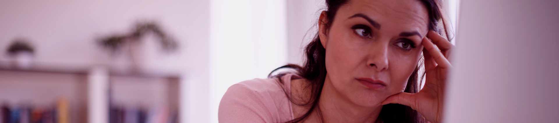 Mulher pensativa em frente ao computador. Parece estar pensando em quem tem acesso a sua internet