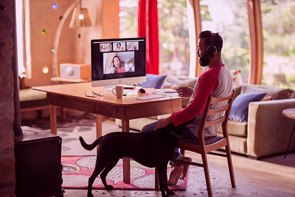 Imagem de um homem participando de uma videochamada em casa, junto de um cachorro.