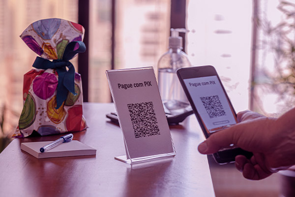 Imagem de uma mão apontando o celular para o Qr-Code para efetuar o pagamento via Pix na loja. 