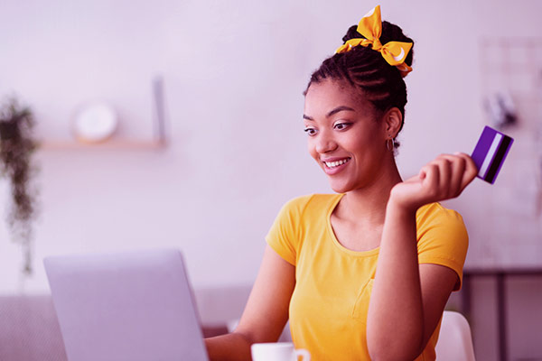 Imagem de uma mulher usando o notebook e segurando um cartão de crédito.