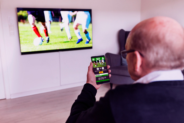 Imagem de um senhor acompanhando futebol pelo celular e pela televisão.