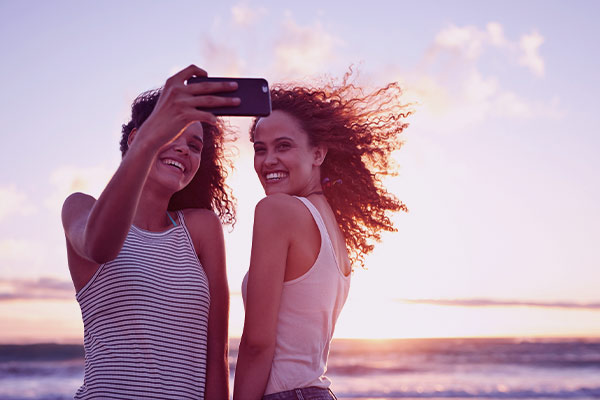 Duas jovem garotas tirando selfie do amanhecer na praia. 