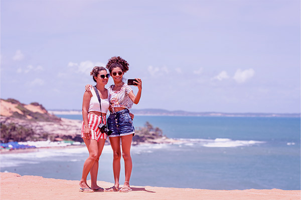Amigas na praia tirando foto delas e o fundo do mar. 