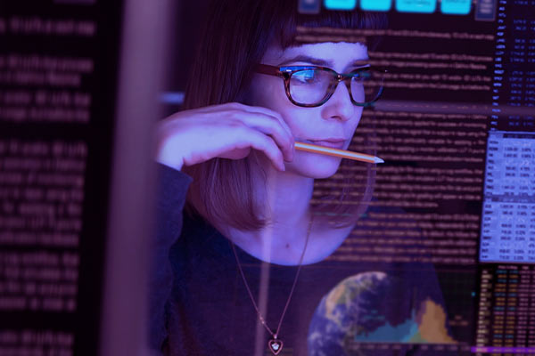 Mulher com um lápis na boca olhando uma tela enquanto hackeia
