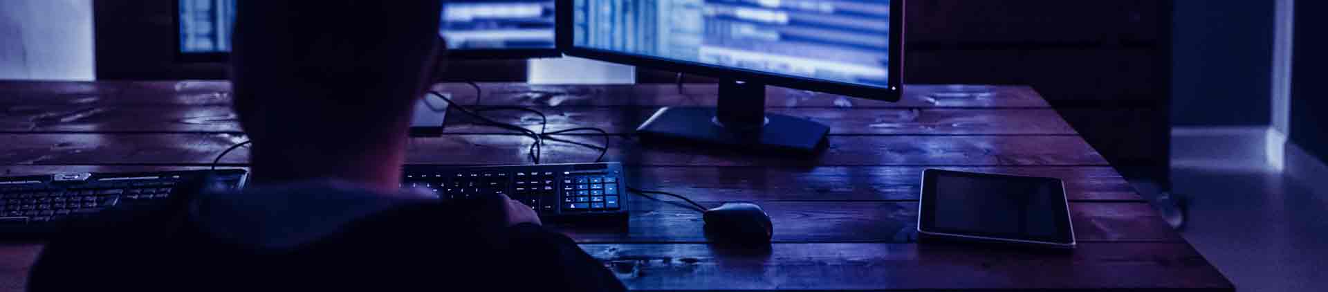 Pessoa mexendo no computador com duas telas, atenta aos números. Ao seu redor, vários gráficos.