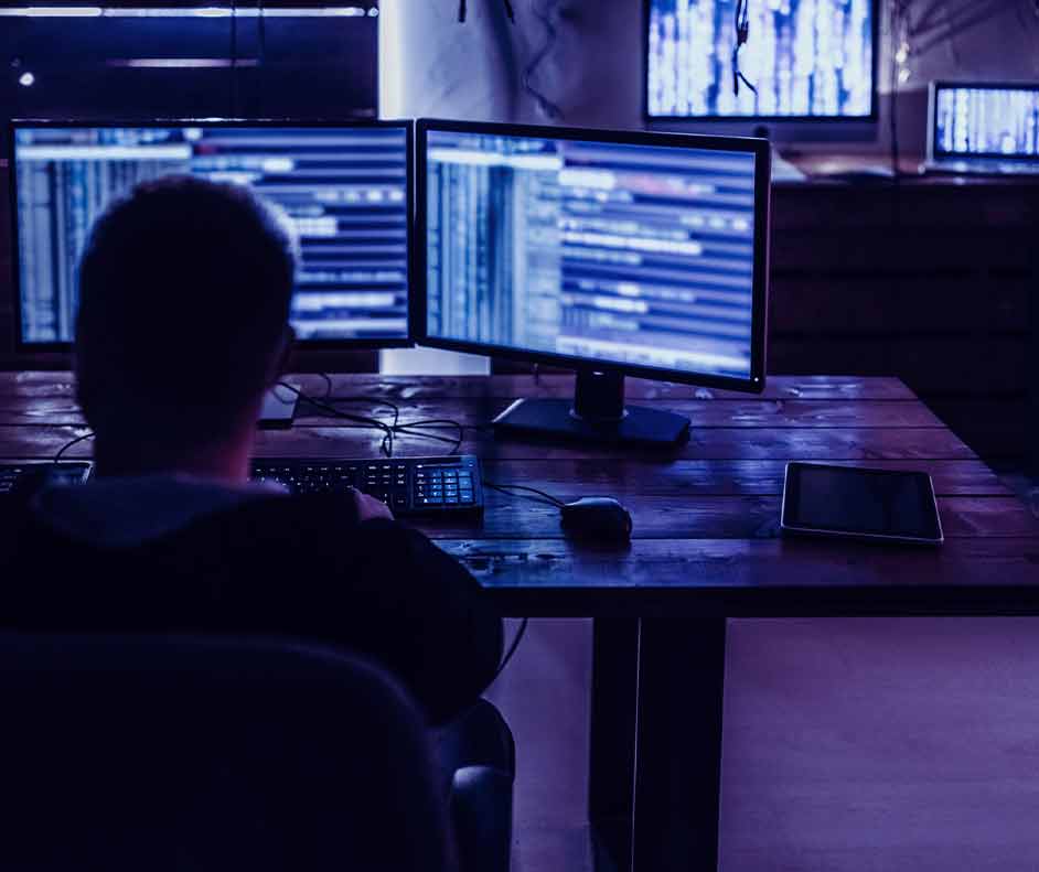 Pessoa mexendo no computador com duas telas, atenta aos números. Ao seu redor, vários gráficos.
