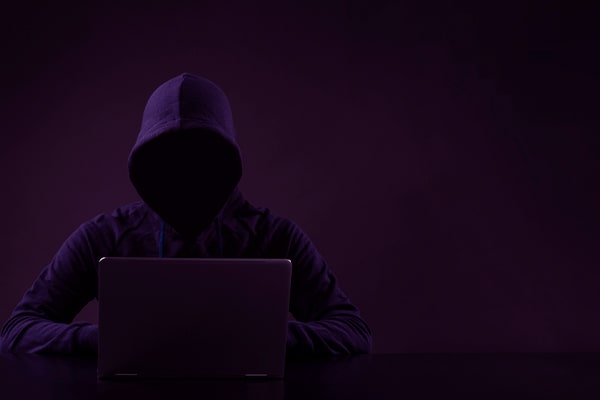 Pessoa usando moletom com capuz e rosto escondido nas sombras usando um computador