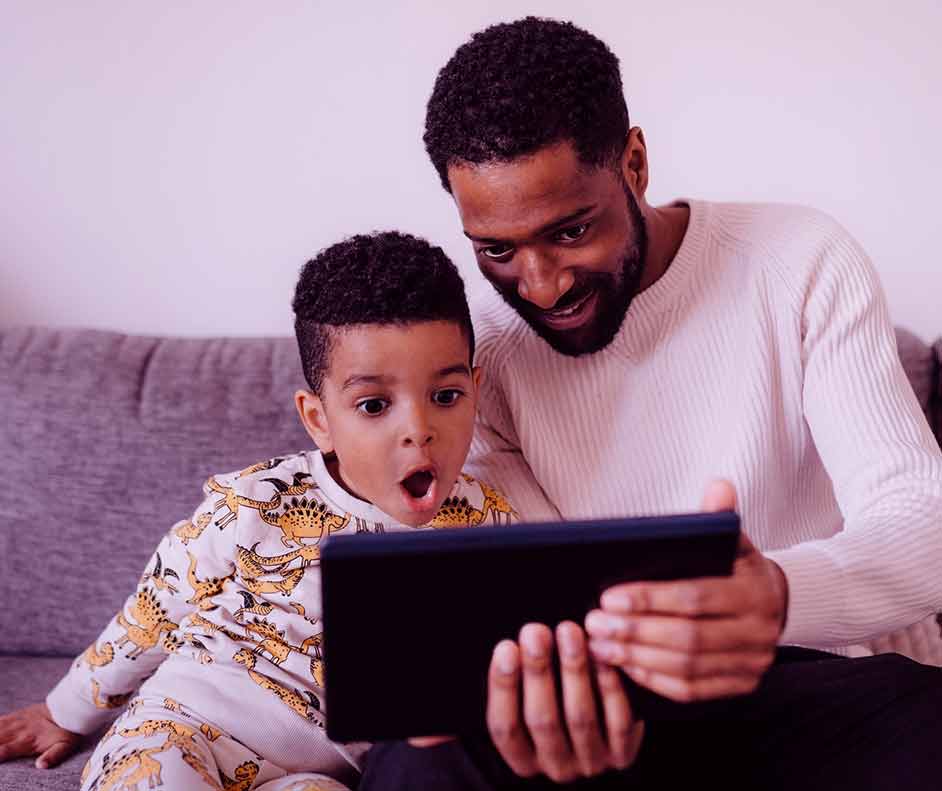 Pai e filho reunidos, sentado em um sofá assistindo os filmes da DC em um tablet