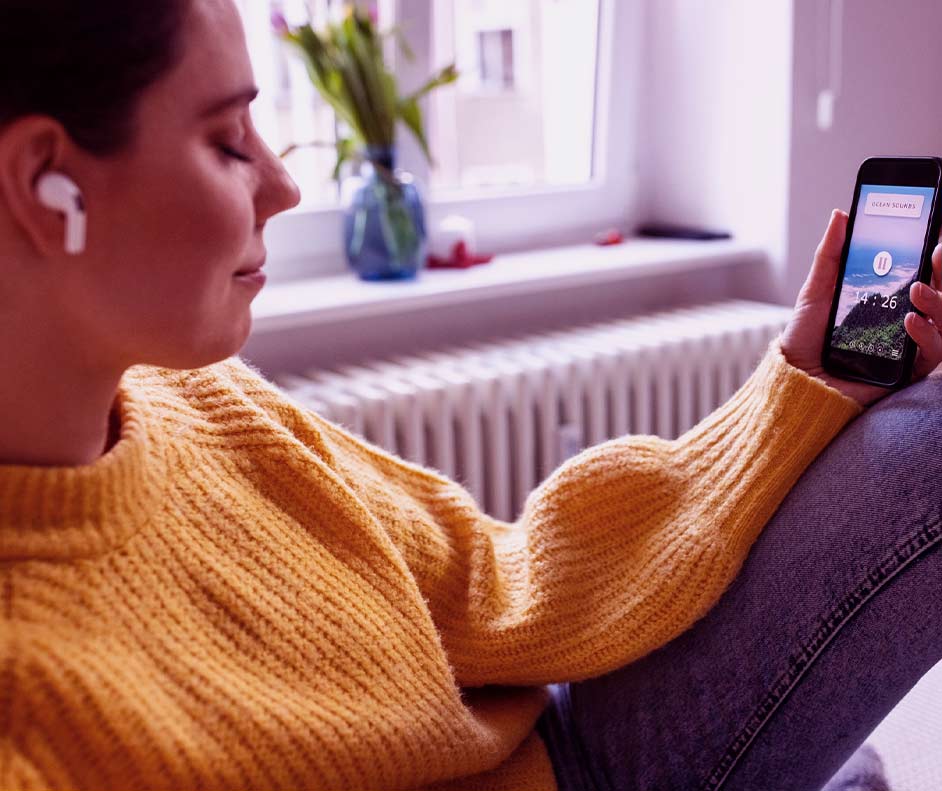 Mulher deitada no sofá de olhos fechados ouvindo música com os melhores fones de ouvido bluetooth