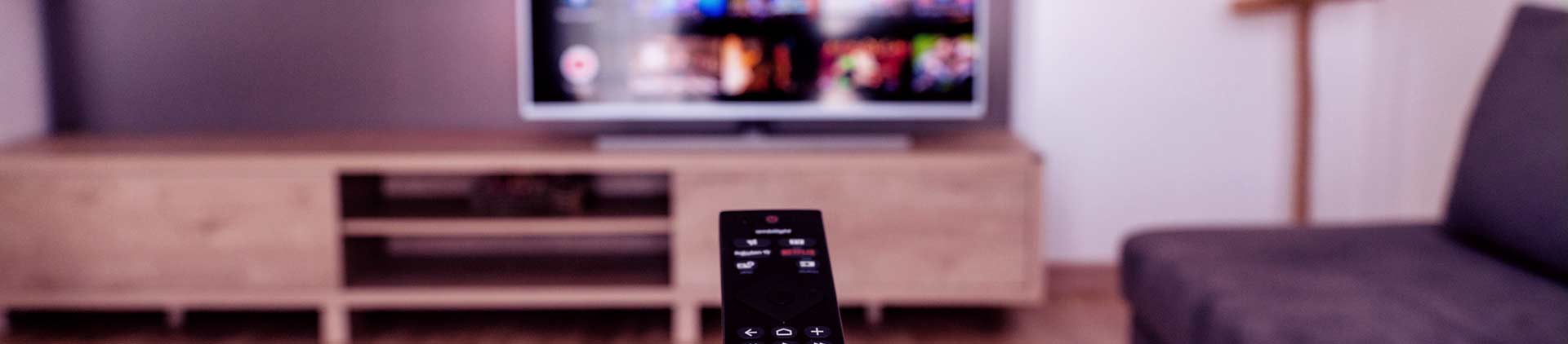Pessoa apontando controle para TV. Na tela, os canais ao vivo da Globoplay desfocados