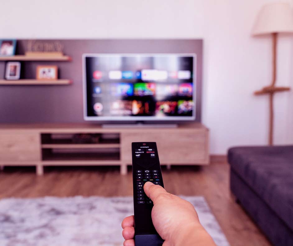 Pessoa apontando controle para TV. Na tela, os canais ao vivo da Globoplay desfocados