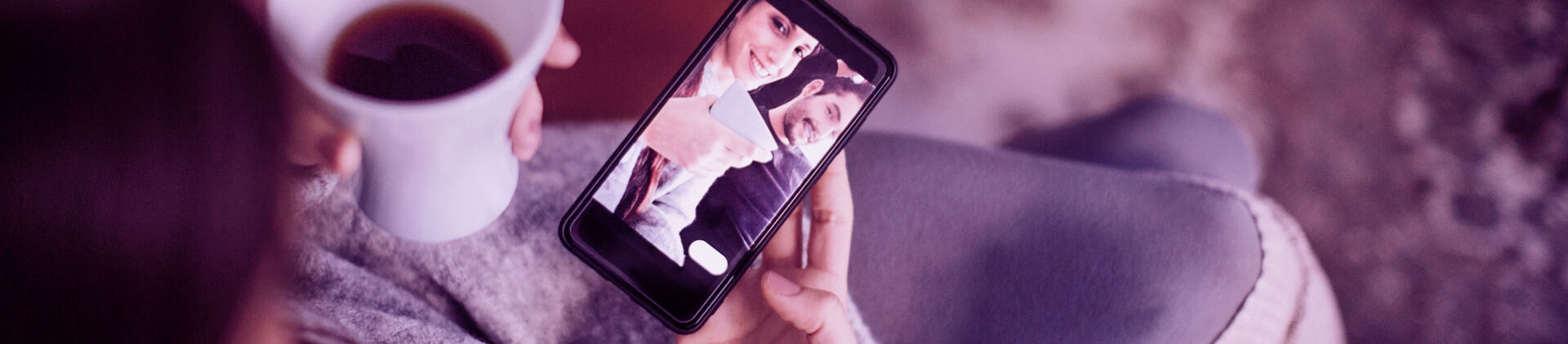 Pessoa segurando o café em uma mão e o celular em outra. Parece que ela está tirando uma selfie.