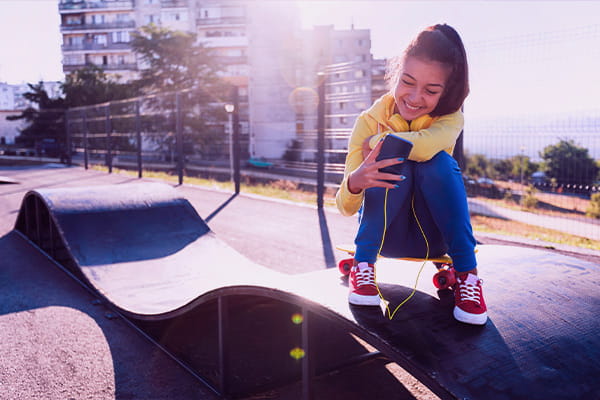 Menina na pista de skate usando o celular com internet para condomínio