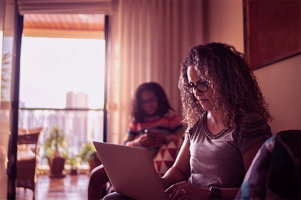 Duas mulheres na sala do apartamento e sentadas no sofá usando notebook e celular