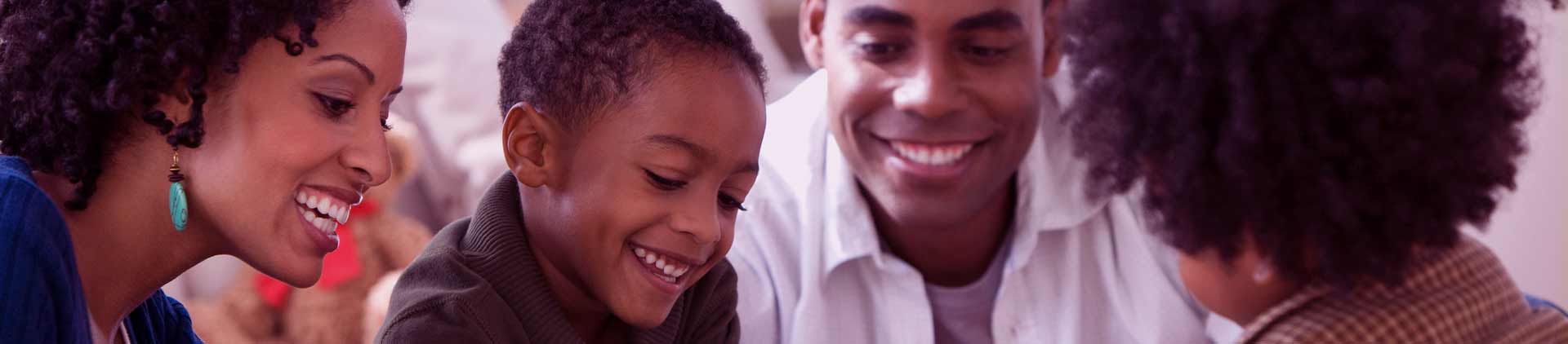Família negra composta por mãe, pai e dois filhos jogando um jogo de tabuleiro em cima da mesa