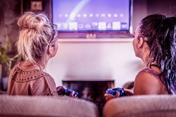 Imagem de duas mulheres de costas no sofá jogando videogame na TV