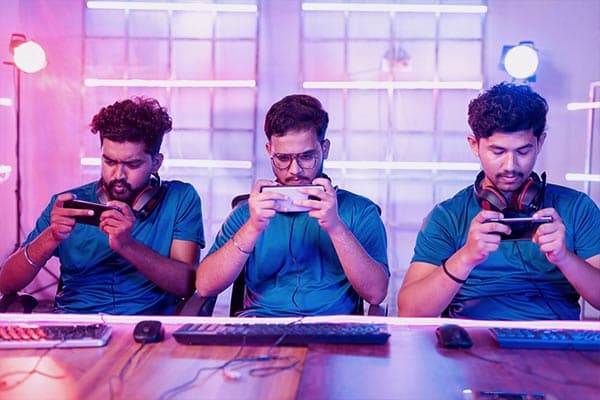 Três jovens usando headsets sentados em uma mesa e jogando no celular