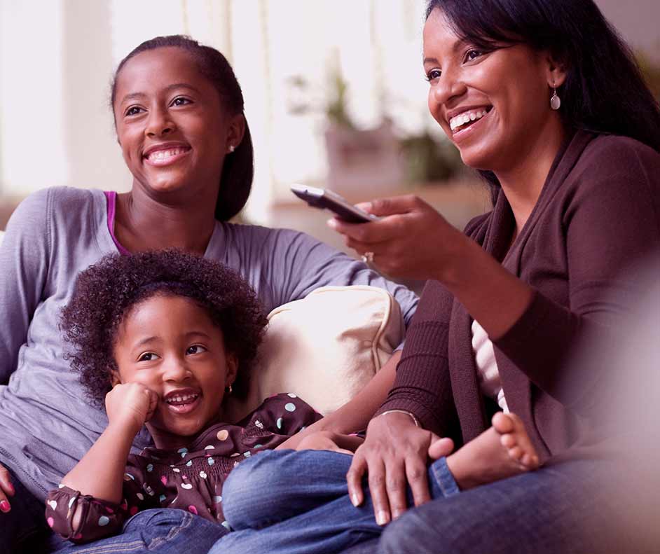 Mãe e filhas reunidas em um sofá e com o controle na mão para assistir os lançamentos Disney