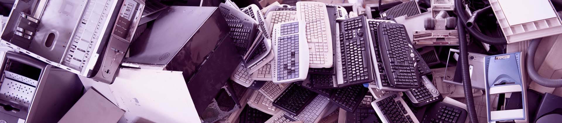 Pilha de lixo eletrônico com diversos teclados e peças de computador descartados.