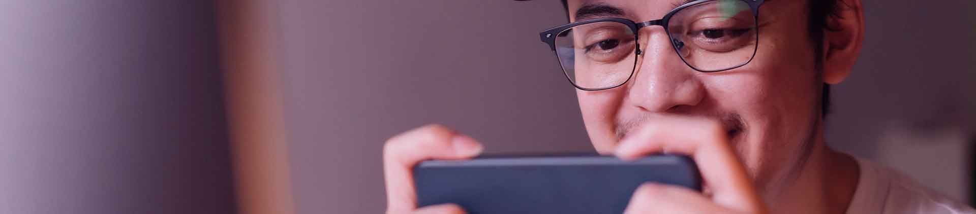 Homem branco de óculos e boné jogando pelo celular por meio da Netflix Games