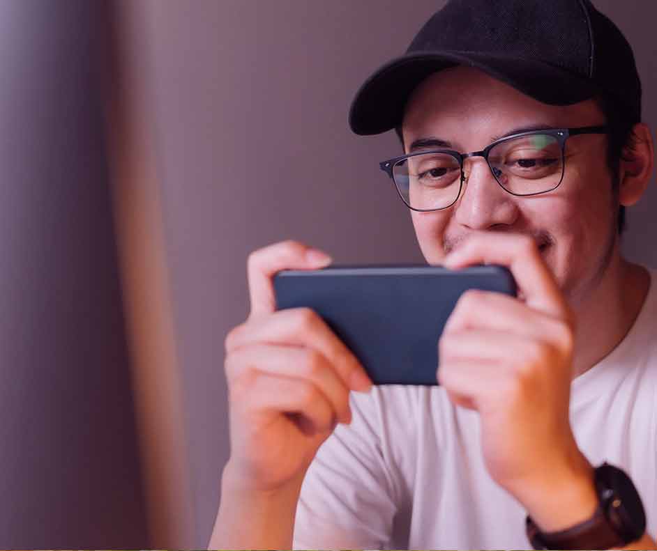 Homem branco de óculos e boné jogando pelo celular por meio da Netflix Games