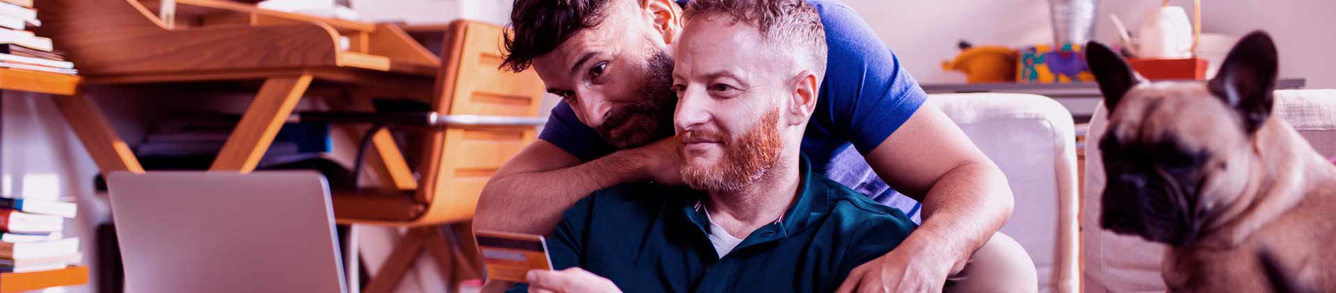 Dois homens abraçados vendo promoções na internet em um PC. Um deles segura um cartão de crédito