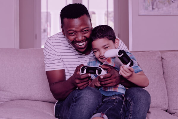 Imagem de pai e filho jogando videogame no sofá de uma sala