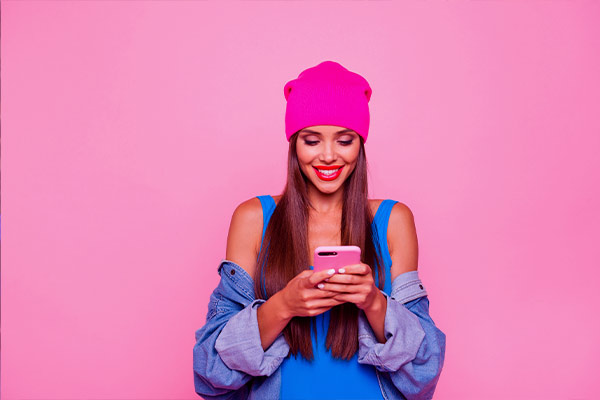Imagem de uma mulher usando um celular em frente a uma parede rosa.