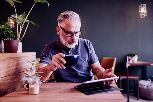 Homem sentado em uma cafeteria com uma xícara na mão e usando um tablet ligado ao wi-fi público