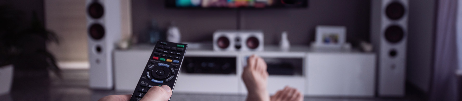 Pessoa segurando controle apontado para TV. Ela vai assistir aos principais serviços de streaming