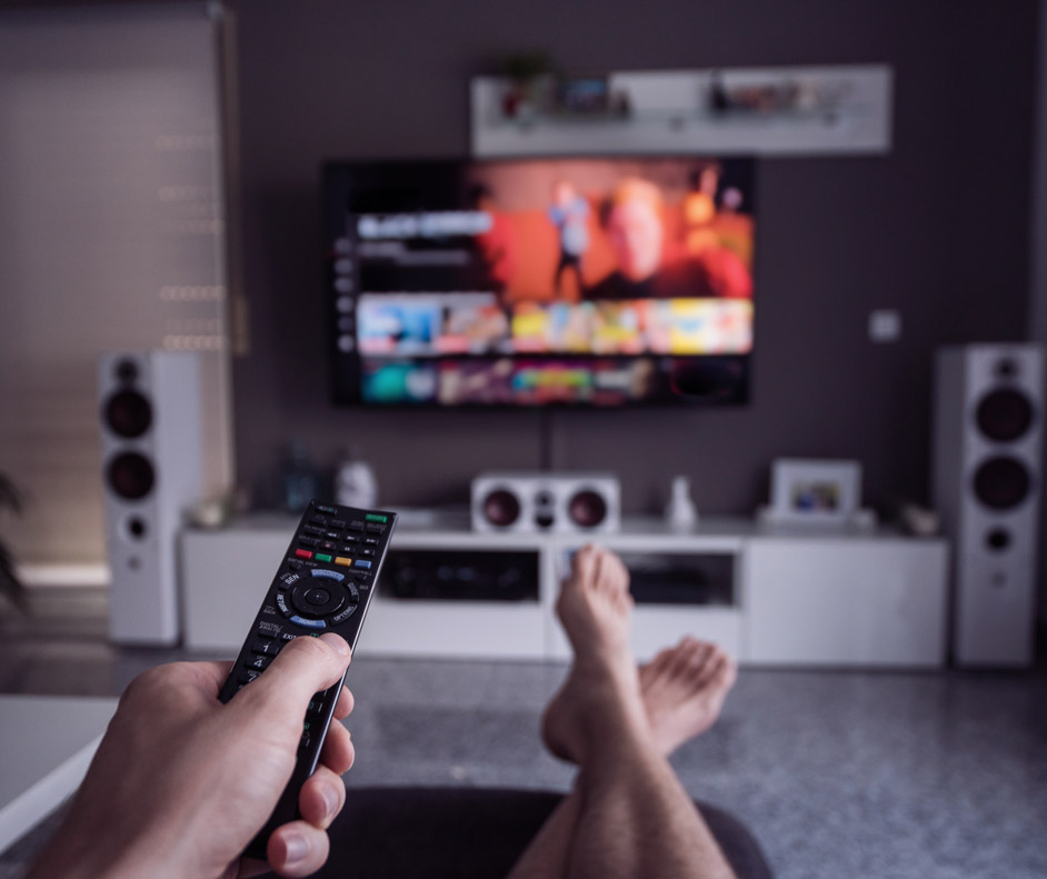 Imagem de uma pessoa no sofá apontando o controle remoto para a TV.